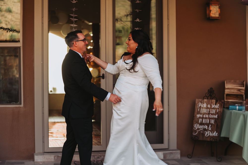 A couple in wedding attire share a joyful moment together on a porch with rustic decor.