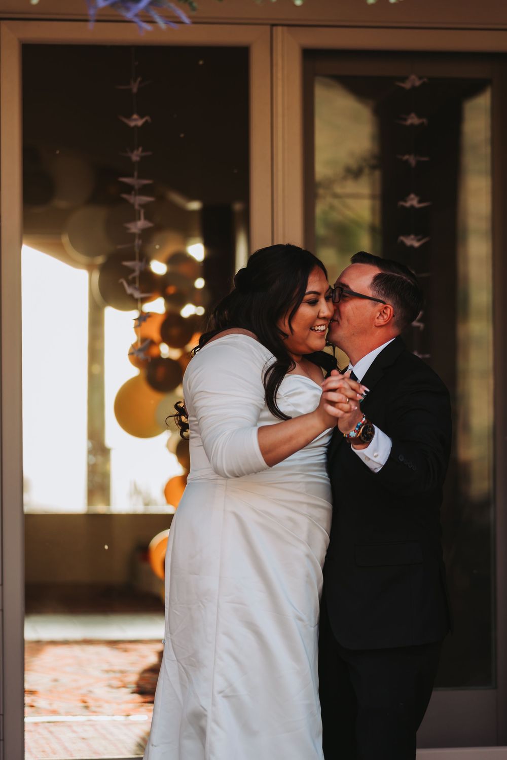A couple dancing together at their wedding reception with orange decorations and paper cranes visible in background.
