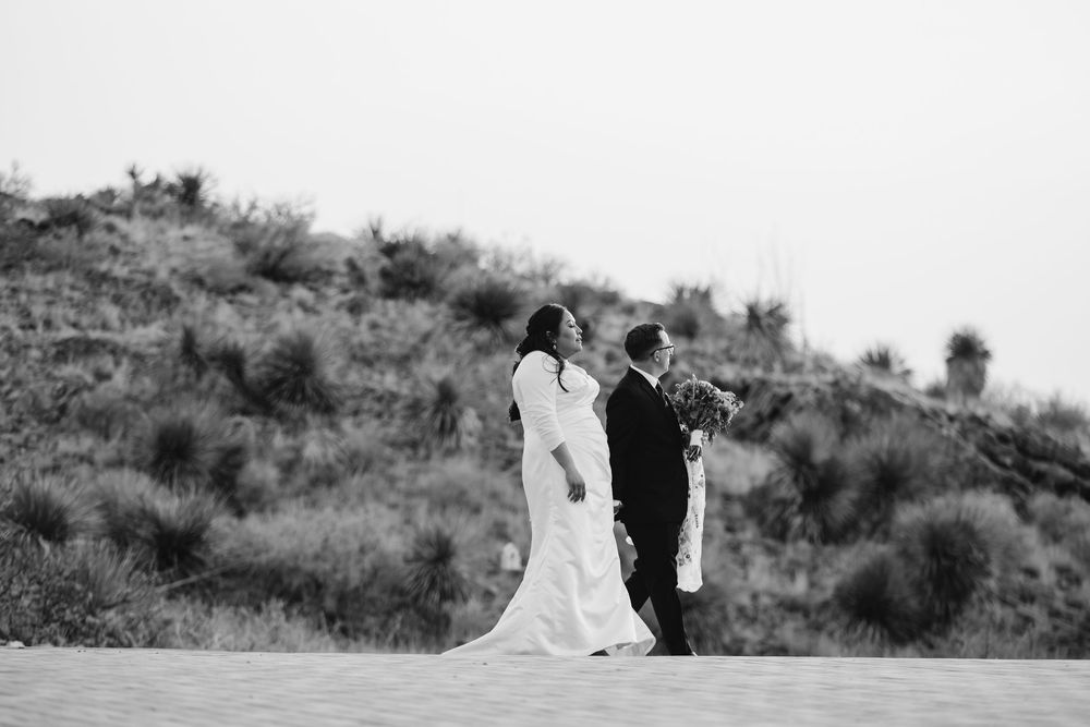 Black and white panoramic wedding photo sequence shows couple posing at sunset in desert terrain with mountains in background.