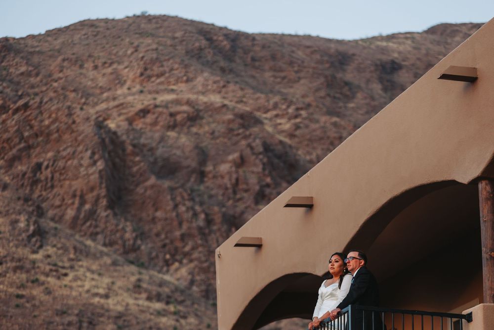 A series of adobe-style buildings nestled against rugged desert mountains during sunset.