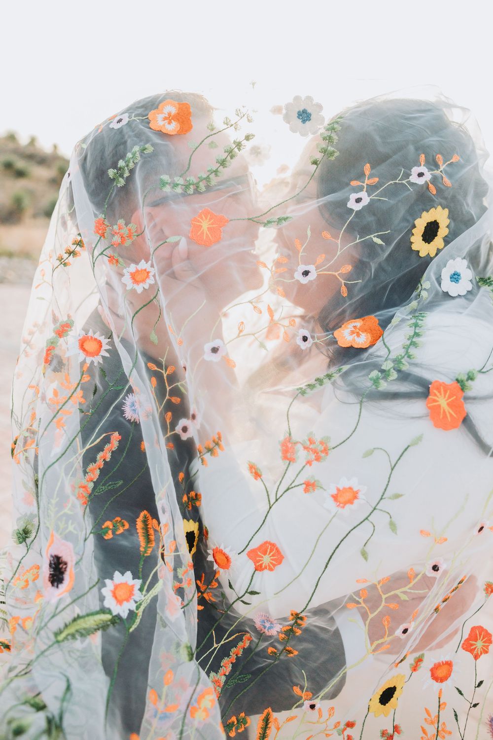 Delicate veil with floral embroidery details in coral and green colors flowing in the breeze.