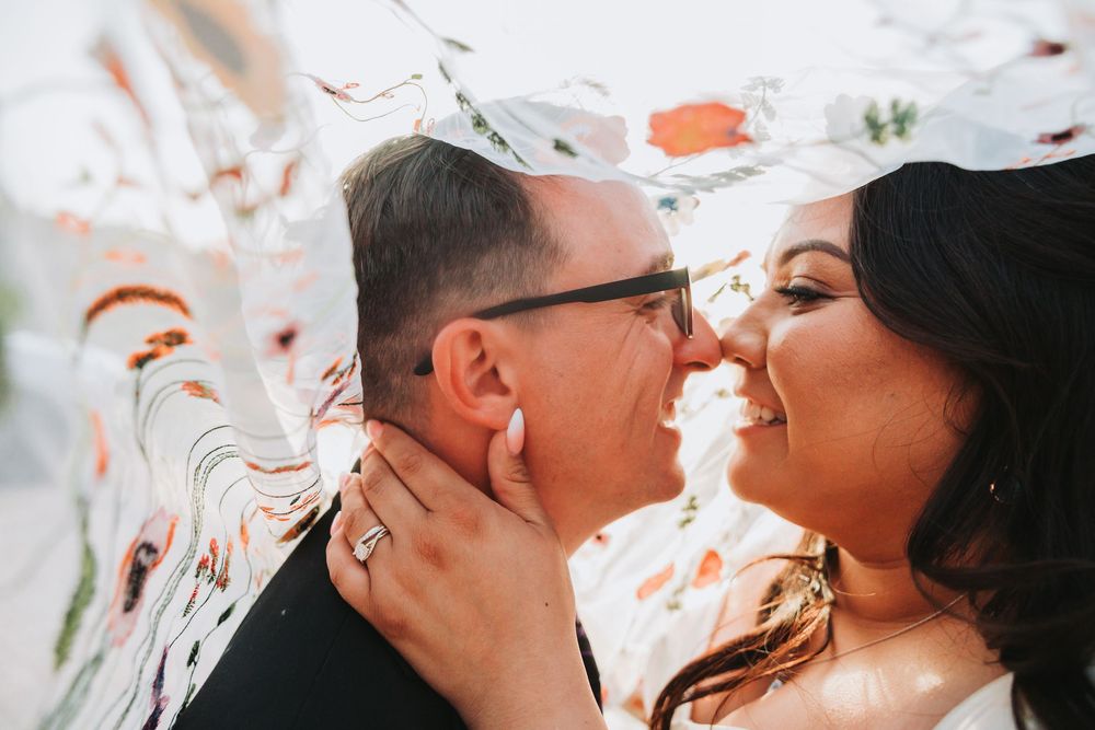 Close-up silhouette of a couple embracing behind a floral embroidered veil.
