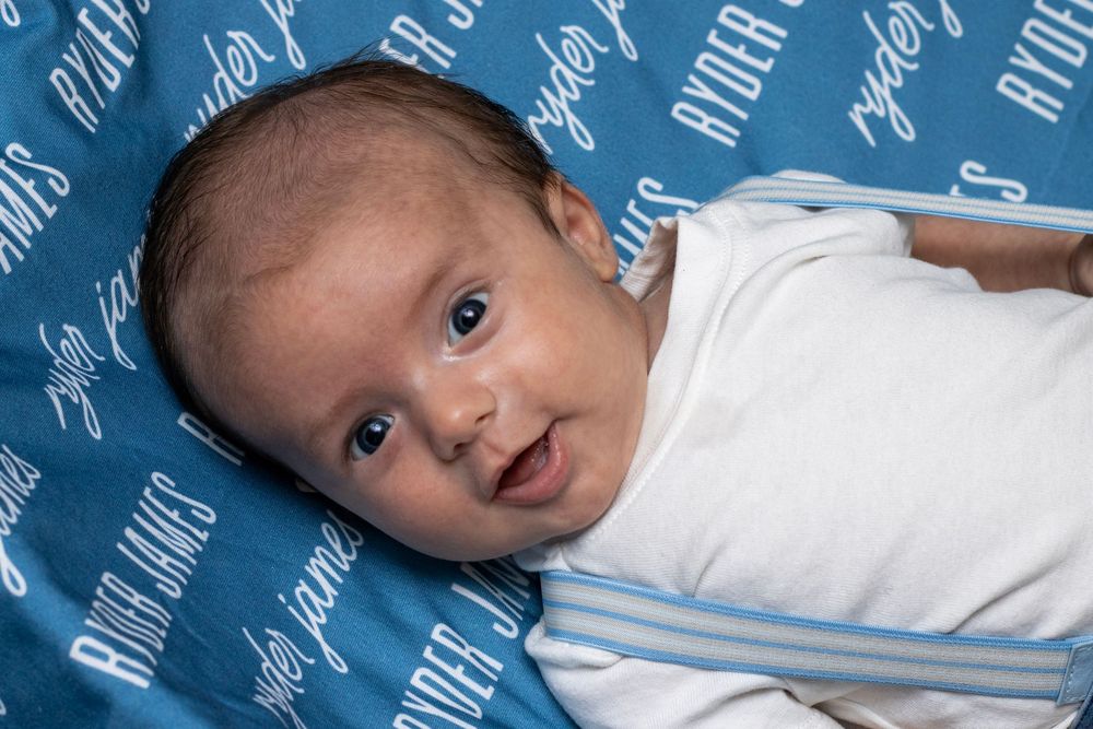 Newborn Photoshoot in South Carolina captures baby in a white onesie lying on a blue patterned blanket.