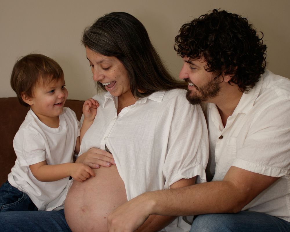 A sequence of tender moments between family members as they interact with a pregnant belly in white clothing.