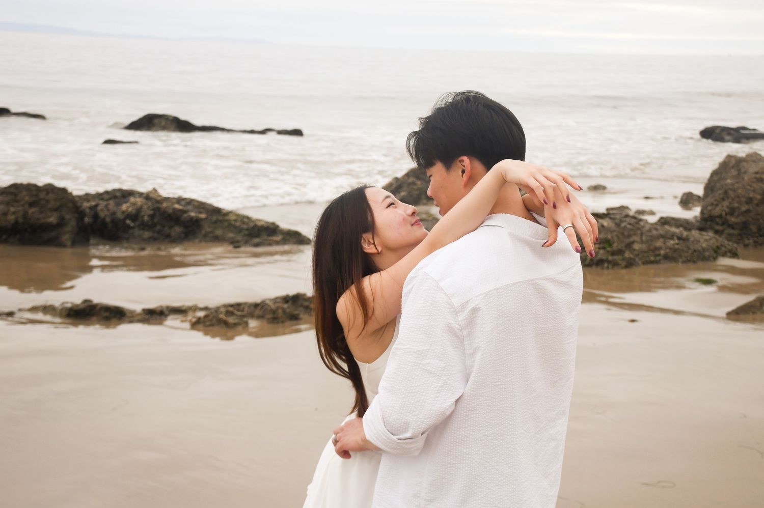Couple sharing a romantic embrace and kiss on a rocky ocean beach.