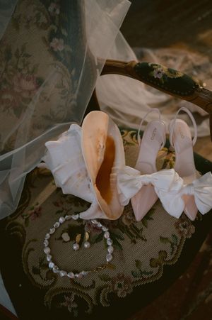 Wedding accessories including ballet flats and pearl details arranged on an antique floral surface.