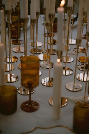 Array of lit white candles in gold holders creating an elegant wedding reception ambiance.