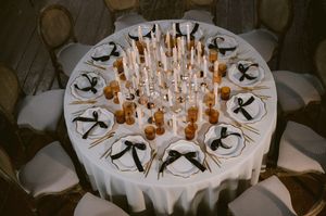 Elegant round dining table set with white linens, glowing candles, and formal place settings for a special event.