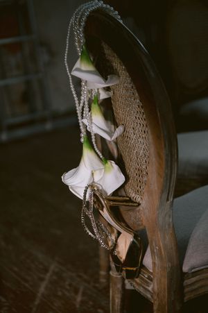 Delicate white flowers and pearl strands draped over an antique wooden chair back.