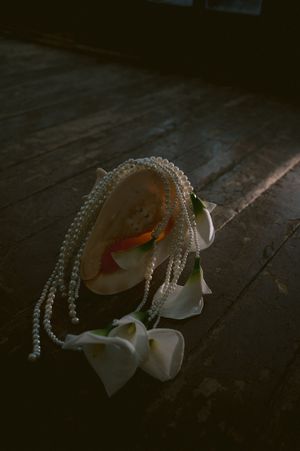 White wedding veil with delicate pearl details lying on dark wooden flooring.