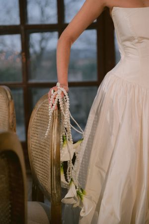 Close-up of white wedding dress details and rattan chair in moody lighting.