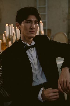 Candlelit portrait of figure in classic tuxedo lounging on antique chair.