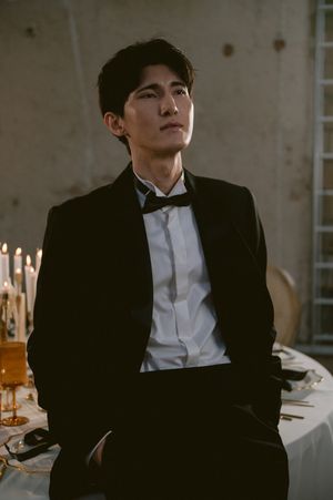 A groom in a classic black tuxedo and bow tie stands elegantly beside a candlelit table at a formal event.
