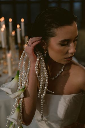 Bride adorned with pearls and white calla lilies in a strapless gown poses by candlelight.