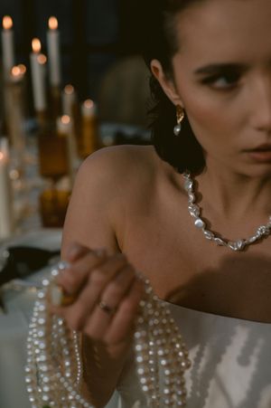 Close-up of bridal jewelry and strapless dress details in romantic candlelit setting.