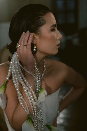 Elegant fashion model in white dress adorned with draped pearl necklaces in a moody evening setting.