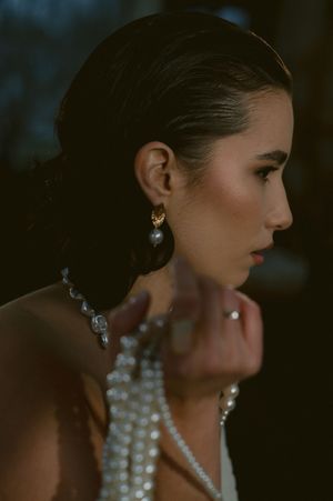 Side profile portrait showcasing elegant pearl jewelry and upswept hairstyle against dark background.