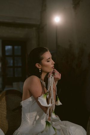 Dramatic side profile of a bride in a white gown wearing pearl jewelry against a dark background.
