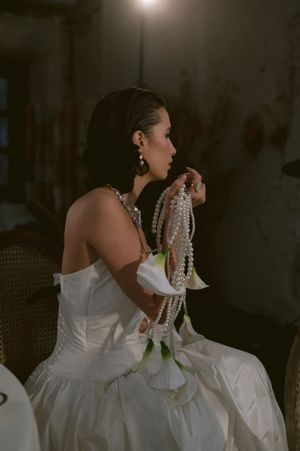 A moody artistic portrait of a bride in a white dress with pearl accessories.