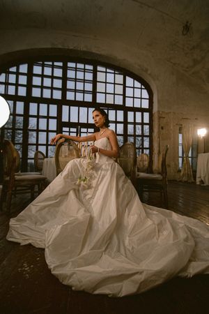 Dramatic bridal portrait with flowing white gown against industrial windows.