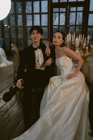 Wedding couple in formal attire posed dramatically in vintage venue with large windows.