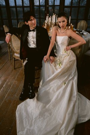 A bride in a strapless white gown and groom in tuxedo pose together in a rustic room with candlelit decor.