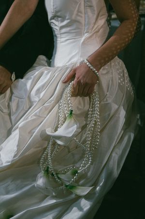 An ornate pearl necklace elegantly draped across the folds of a white wedding gown with crystal embellishments.