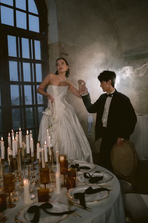 Romantic candlelit dinner scene at dark table with people in formal attire dancing in moody atmospheric lighting.