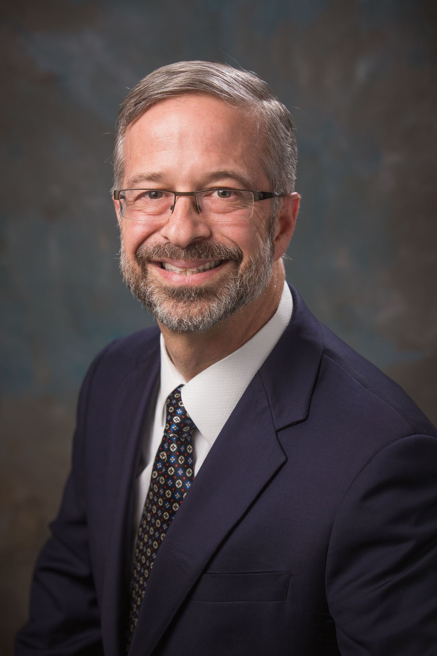 Professional portrait series of person in dark suit with patterned tie against textured backdrop.