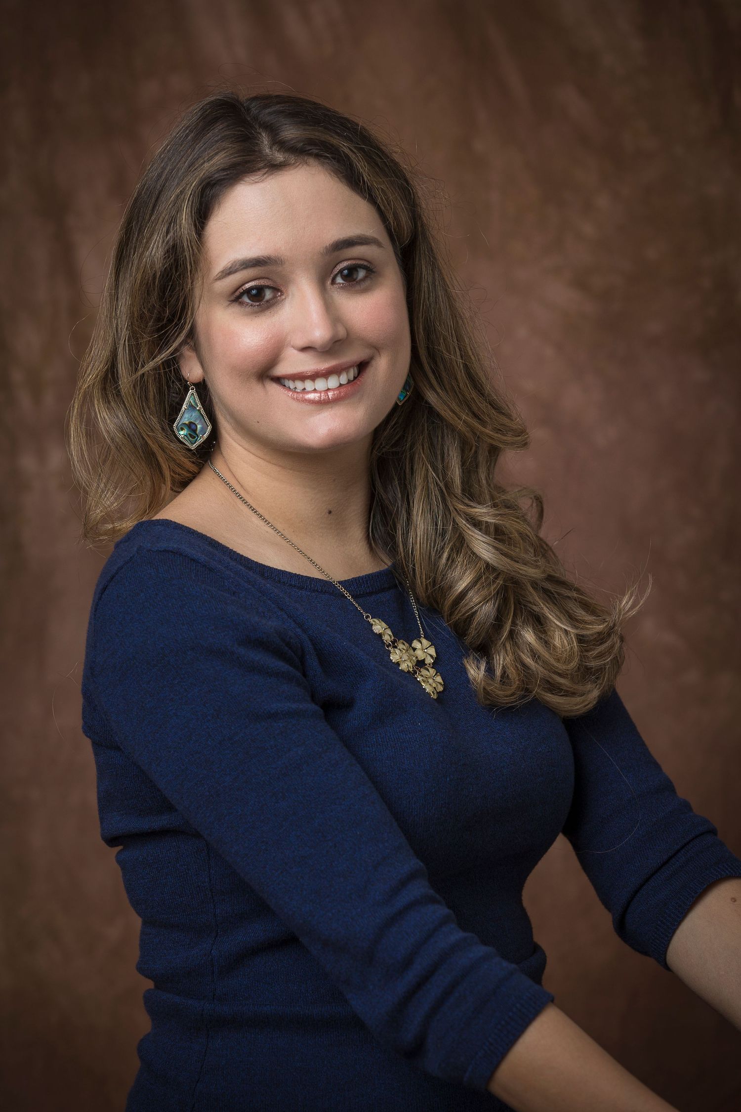 Portrait series of person in navy sweater with jewelry against brown backdrop.