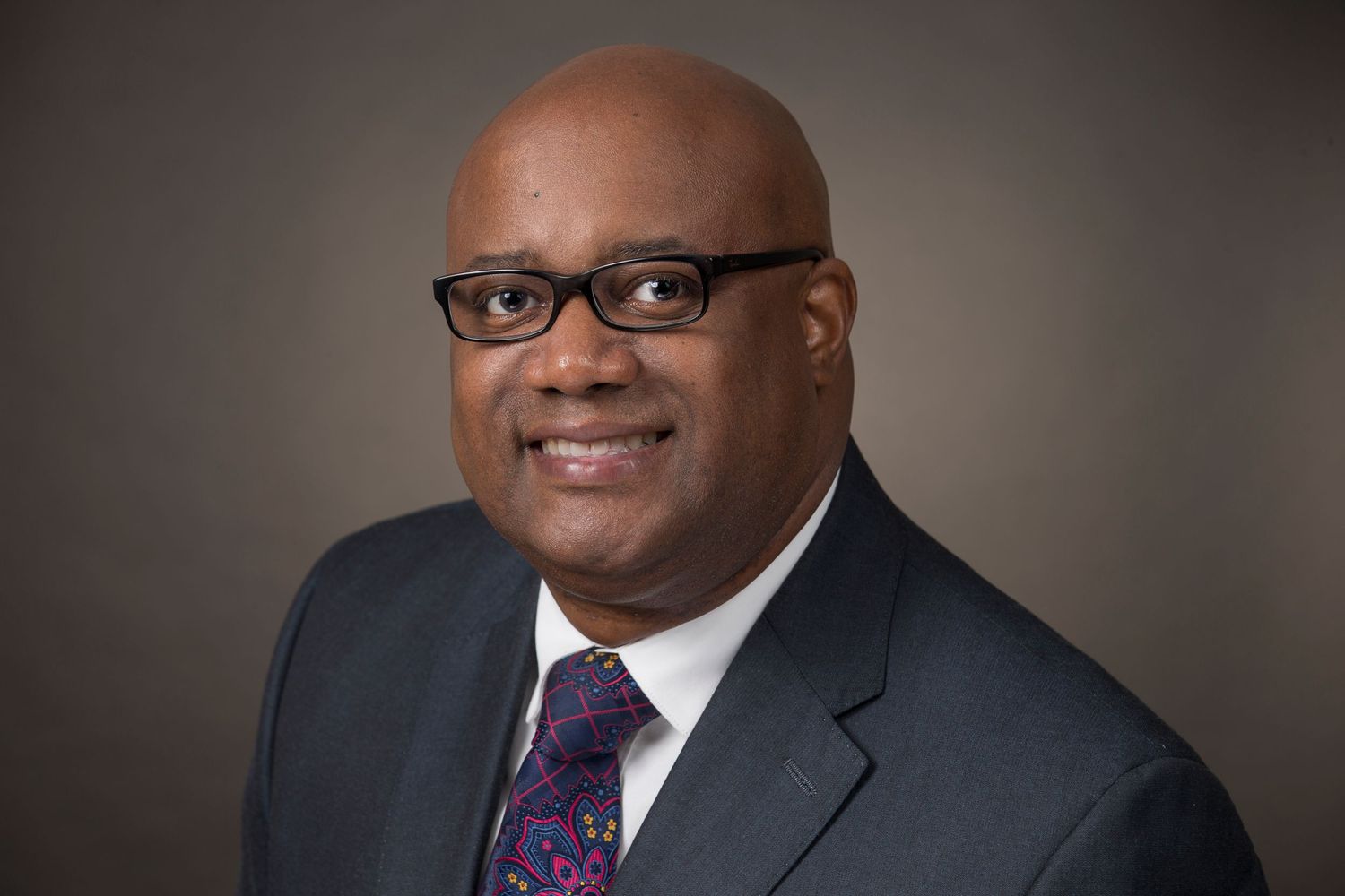 Professional headshot series of person in dark suit and purple tie against neutral background.