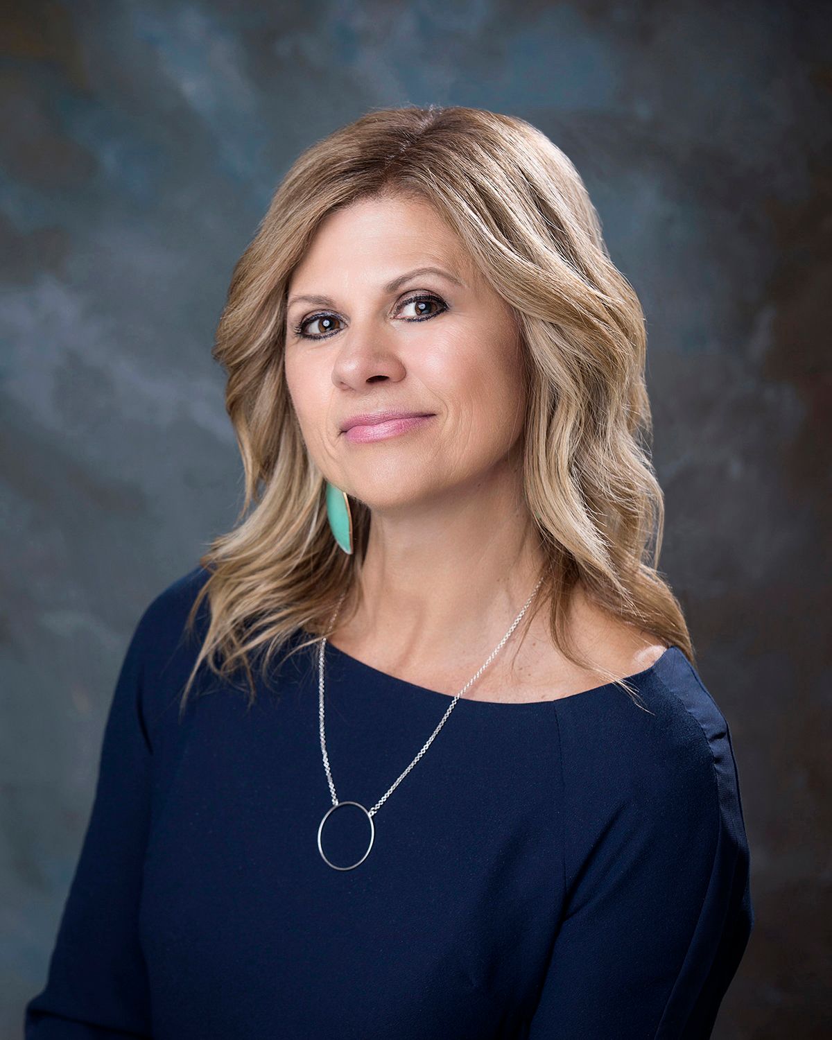 Professional headshot series of person in navy top with statement necklace against dark background.