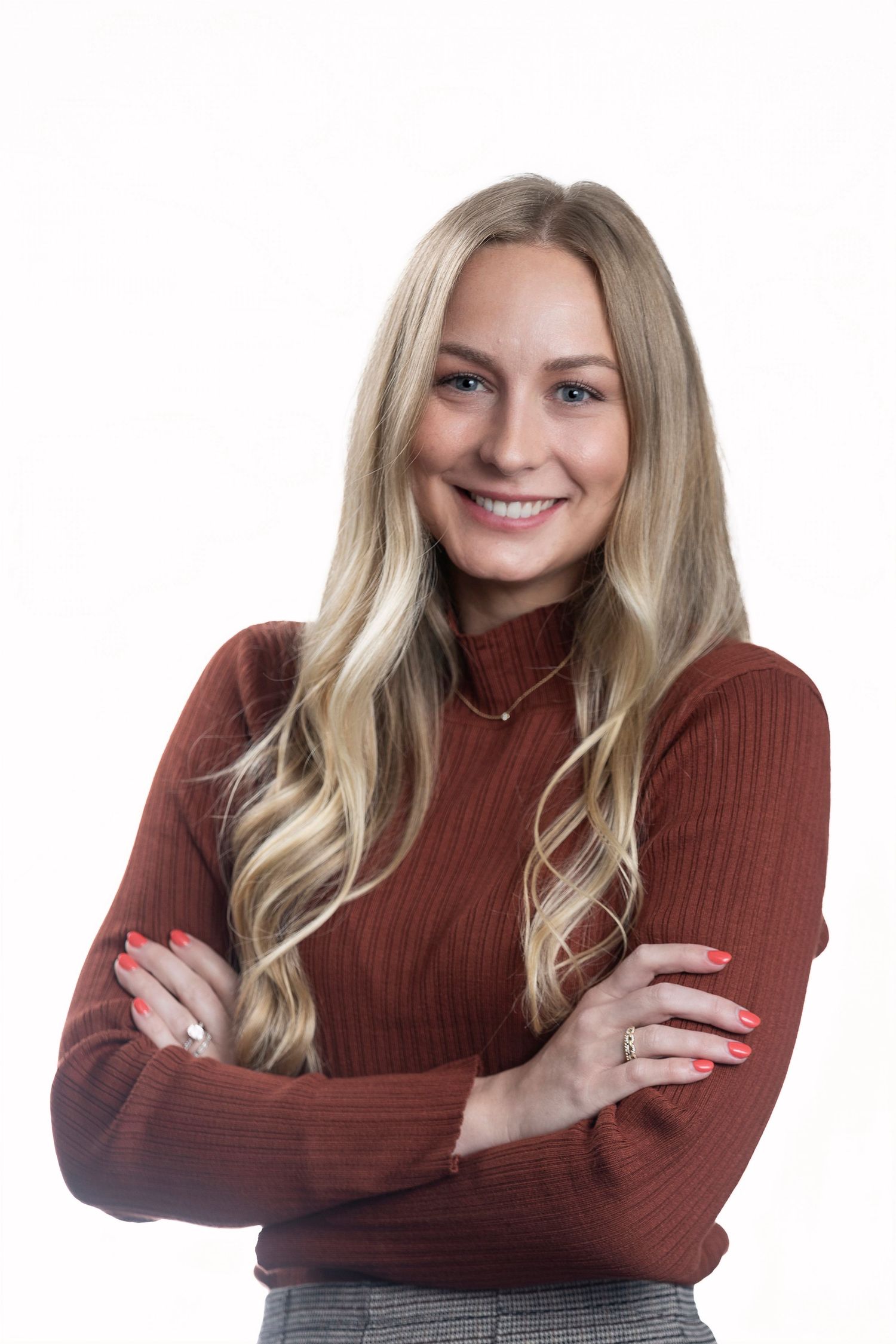Professional portrait of a person in a brown sweater with long blonde hair against white background.