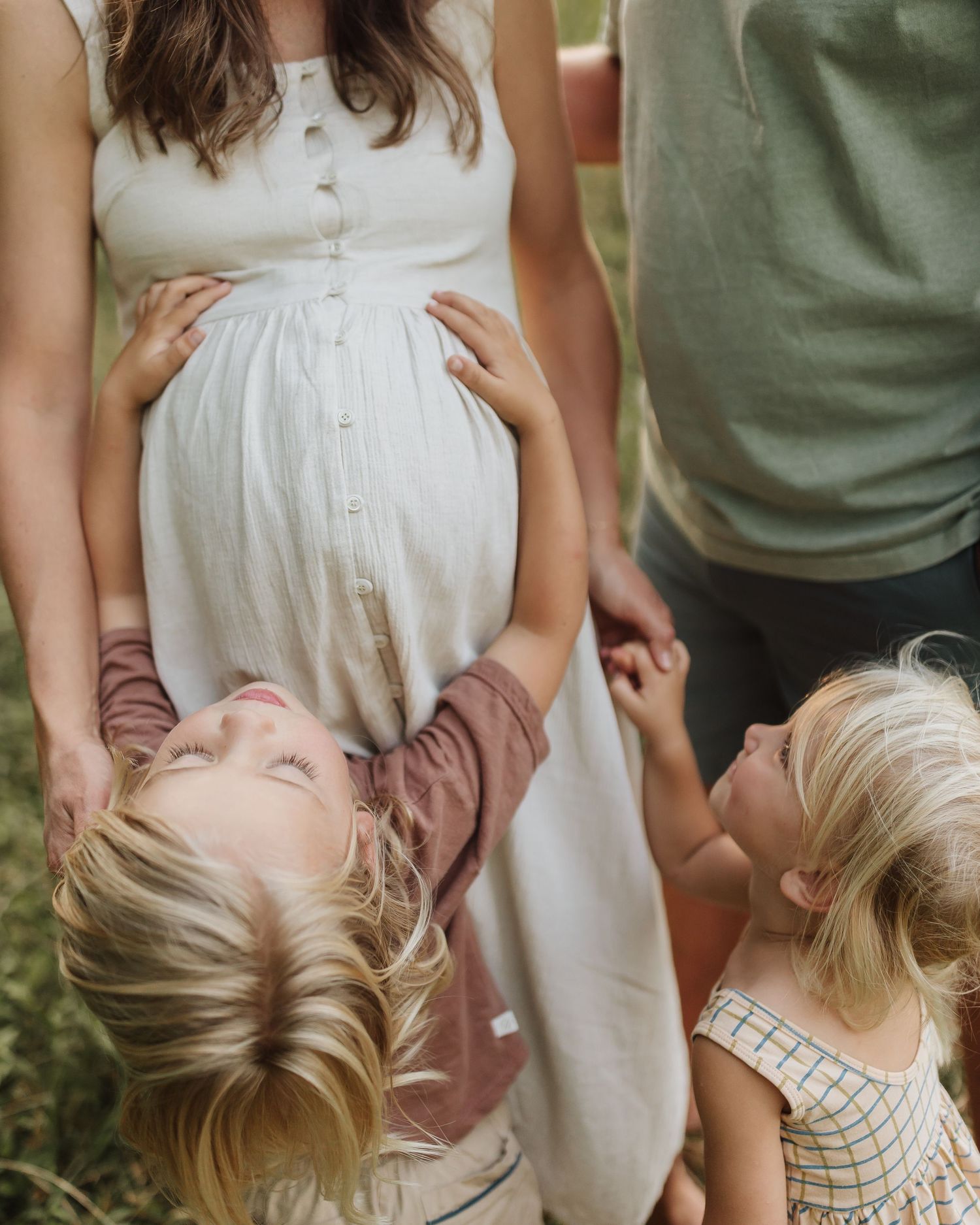 Children playfully interact with a woman in a white dress while enjoying family time outdoors.