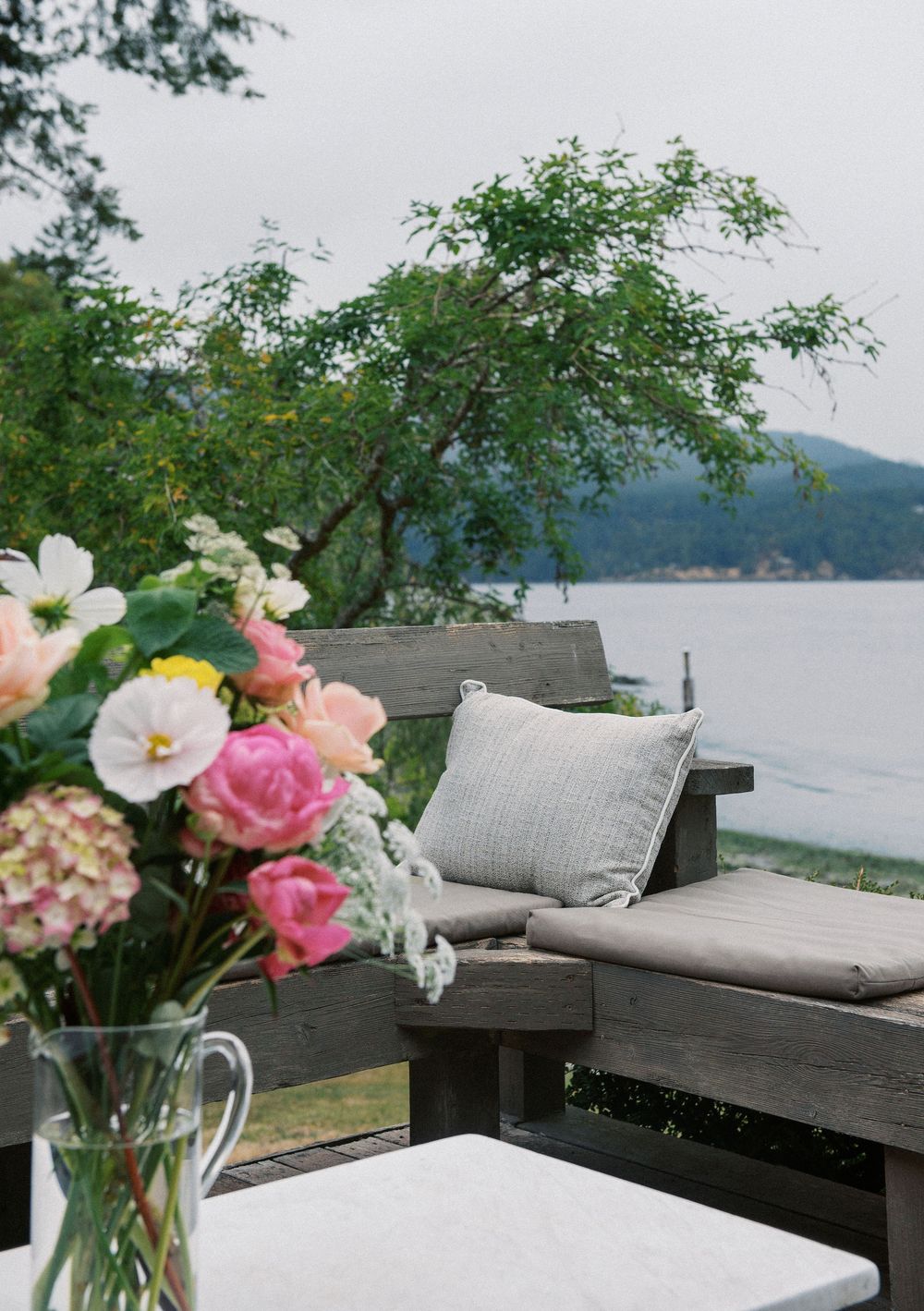 Peaceful waterfront seating area with flowers and cushions overlooking the bay.