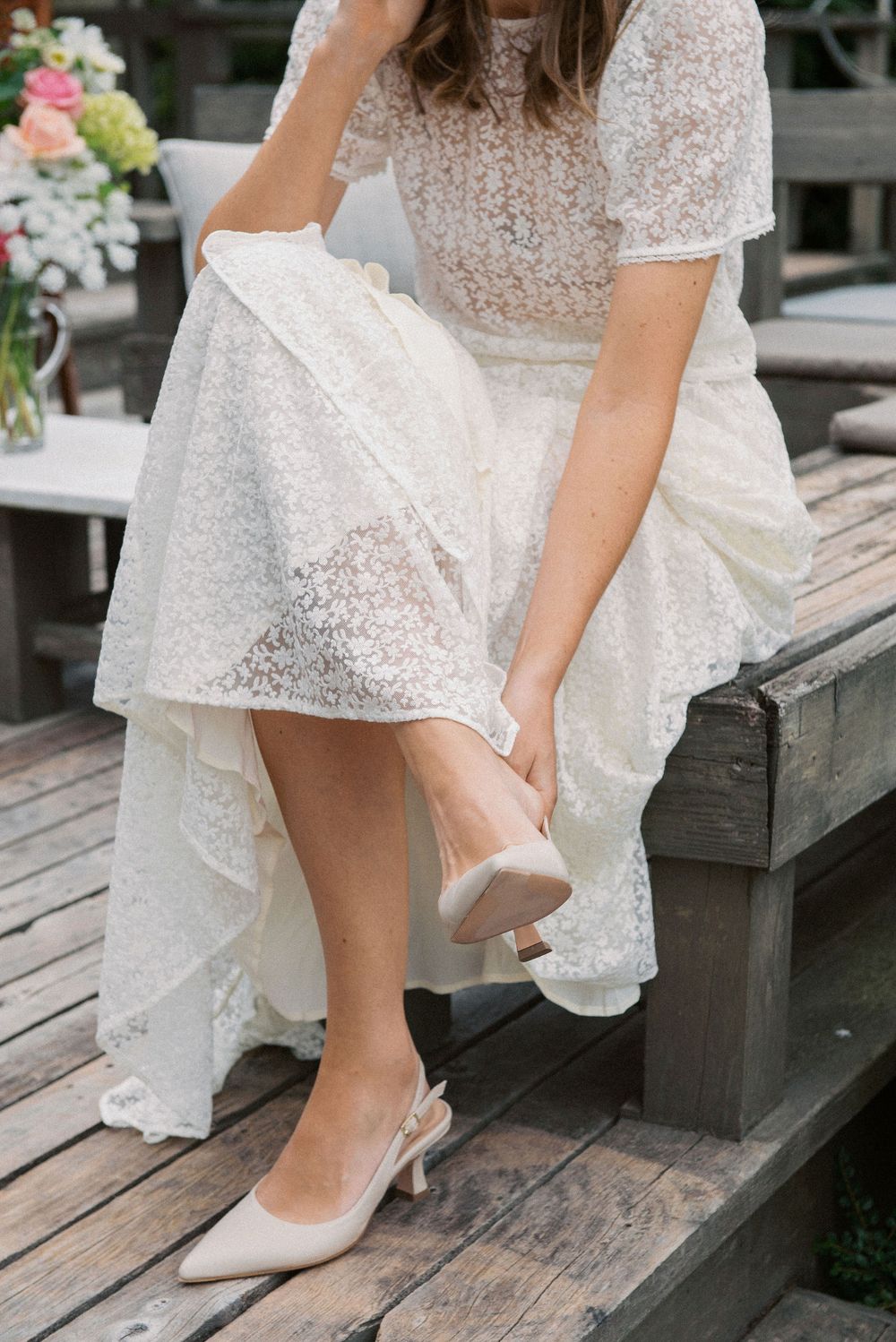Detail of lace wedding dress and white heels on wooden steps.