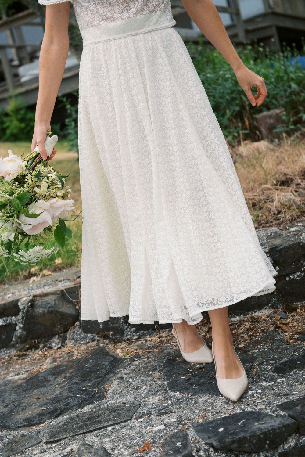 Delicate white lace dress and heels shown in detail against weathered stone steps.