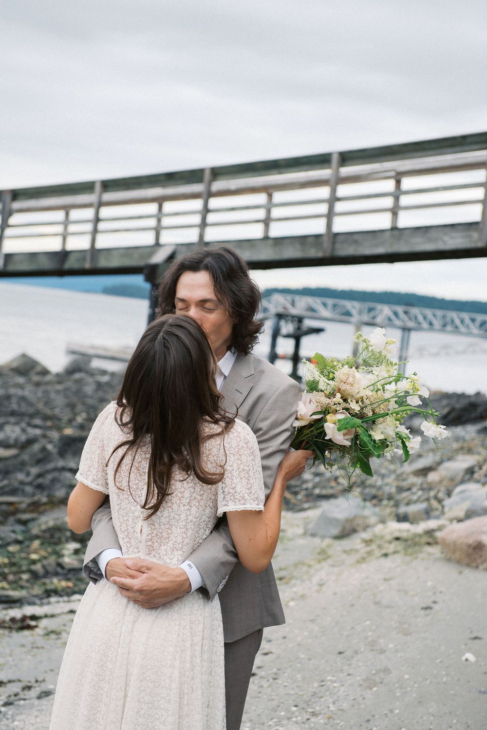 Romantic coastal wedding scene with wooden pier and rocky beach background.