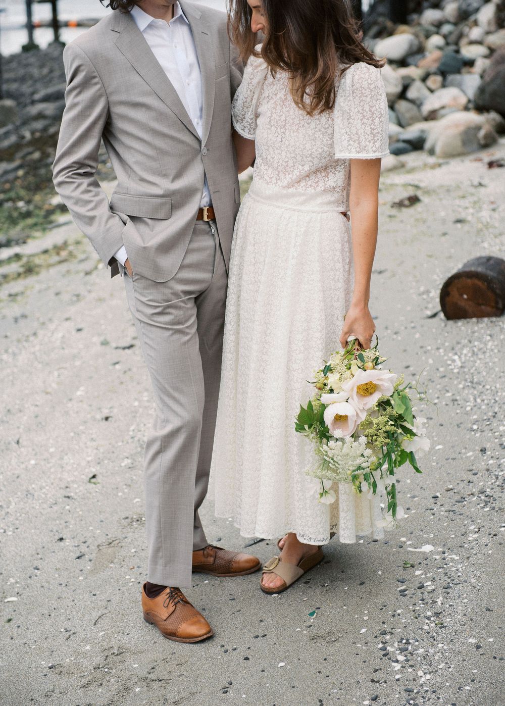 Wedding couple's feet and formal attire photographed on rocky beach.