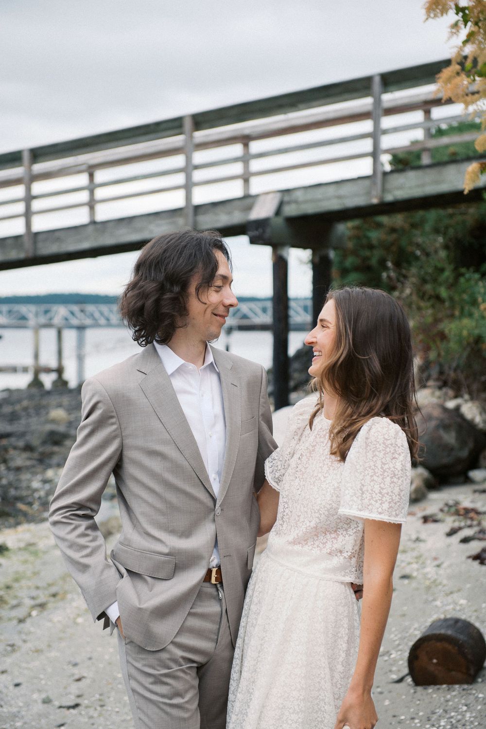 Intimate wedding moment captured on rocky beach with pier backdrop.