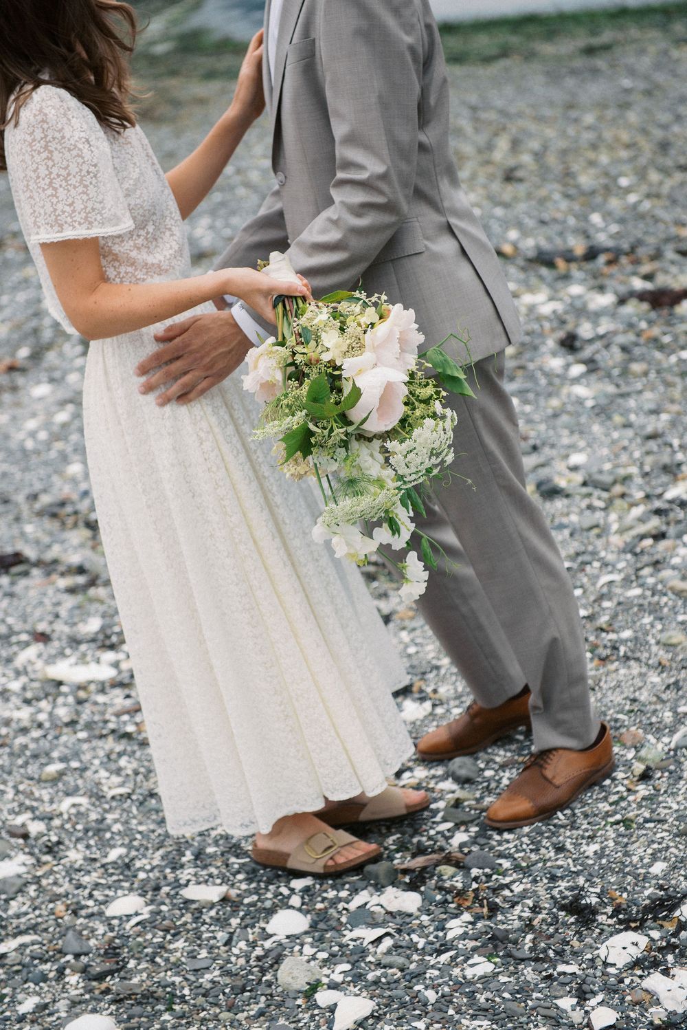 Wedding detail shots focusing on footwear and dress hem against rocky beach backdrop.