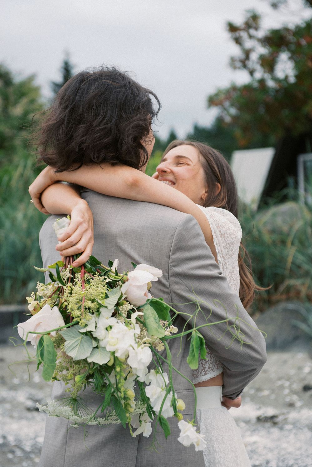 Romantic embrace with white floral bouquet against rocky beach landscape.