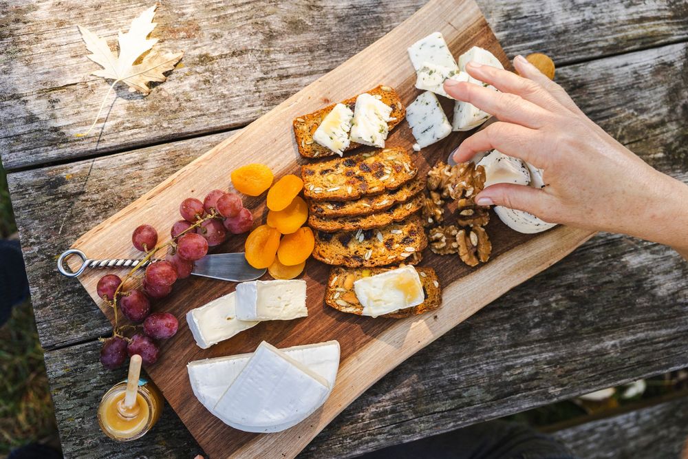 Rustic wooden charcuterie board with assorted cheeses, fruits, and snacks being served outdoors.