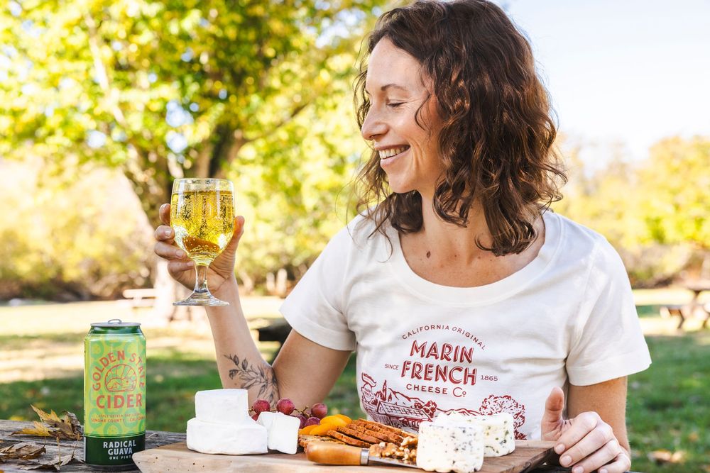 Someone enjoys a craft beer and snacks while sitting outdoors in a sunny park setting.