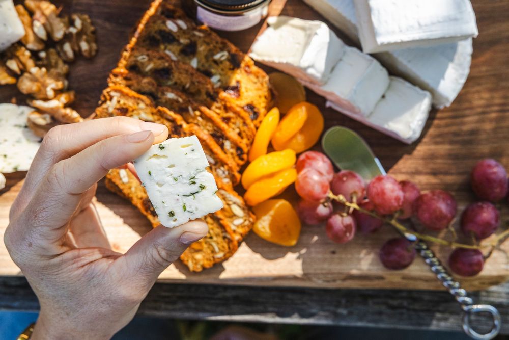Hands reaching for artisanal cheese and crackers on rustic wooden charcuterie board with grapes.
