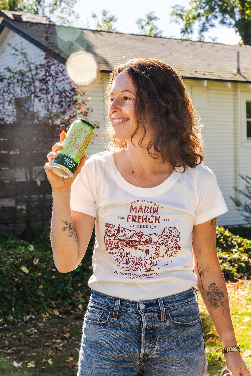 Person wearing vintage-style French graphic t-shirt and jeans poses in sunlit backyard setting.