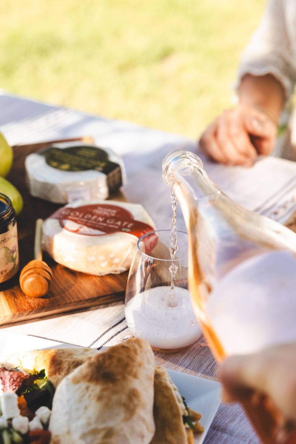 Hands preparing fresh ingredients and assembling sandwiches on a rustic wooden cutting board in natural light.