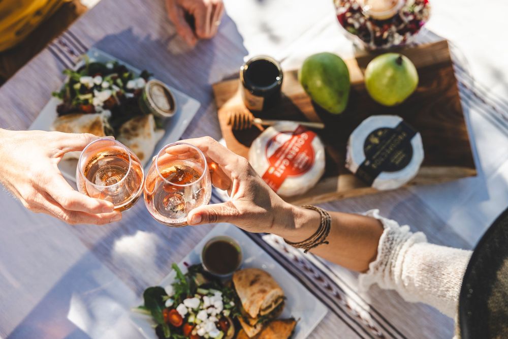 Hands pouring and serving rose wine in elegant glasses at an outdoor dining table setting.