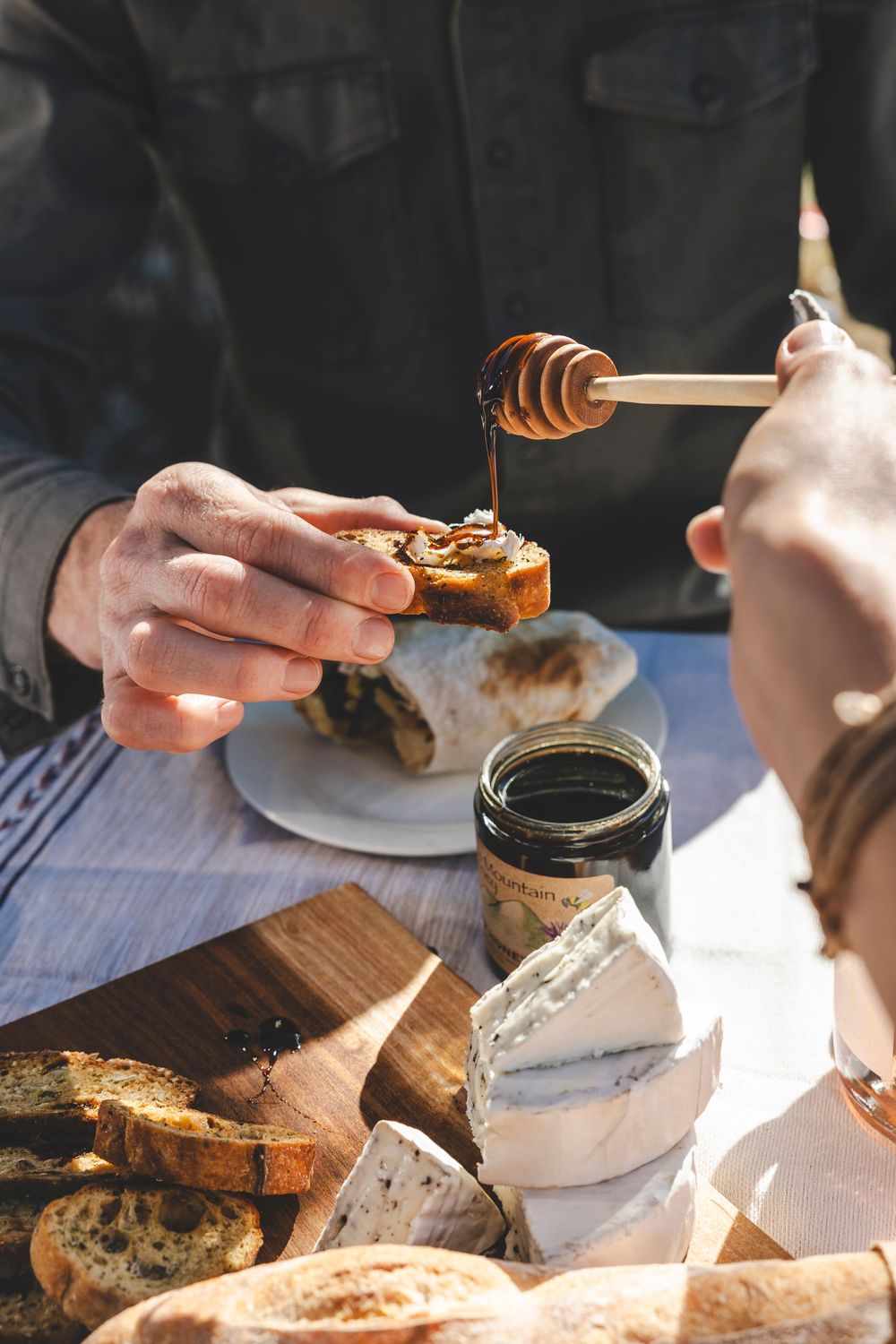 Close-up of hands drizzling honey onto bread slices during sandwich preparation on a wooden surface.