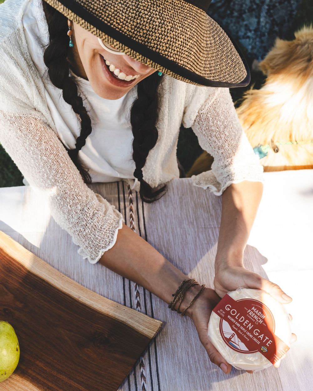 Person in white dress and straw hat slicing fresh citrus fruits on wooden cutting board in kitchen.